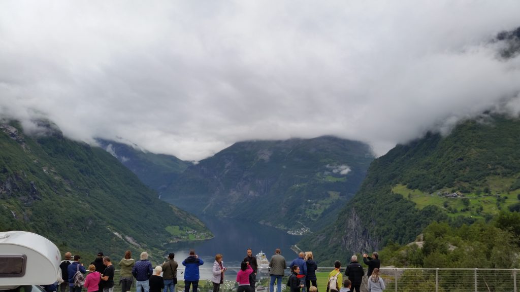 Turisti vestiti a strati sulla terrazza panoramica sopra Geiranger durante una crociera nei fiordi norvegesi